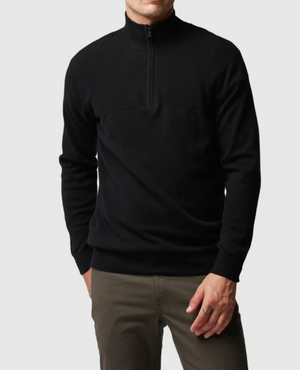 A man in olive pants wearing a black Rodd & Gunn Little Mount Allan Knit with ribbed shoulder and collar texture, stands against a plain light background.