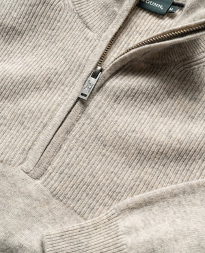 Close-up image of the Rodd & Gunn Little Mount Allan Knit, a beige ribbed-knit pullover featuring a quarter-zip design. The zipper is partially open, revealing a tag on the inside collar with the brand logo and size "M". The texture of the Australian Merino wool and the detail of the stitching are clearly visible.