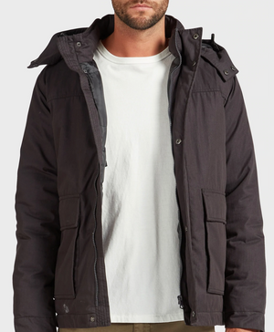 A man stands against a light background, his face partially out of frame, wearing the Academy Brand Miller Jacket over a plain white t-shirt.