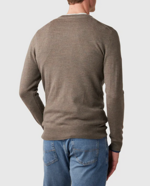 The individual is wearing a Rodd & Gunn Abberfield Knit in brown, made from luxurious Australian Merino Wool with ribbed cuffs and hem, paired with blue jeans. Facing away from the camera, they stand against a plain white background.