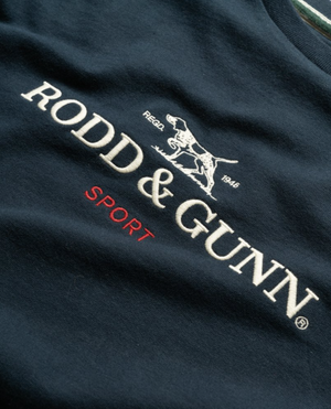 Close-up of the Rodd & Gunn Grenada North Sweat, a navy blue 100% cotton garment featuring the brand "Rodd & Gunn", a logo of a pointer dog, and the words "Regd. 1946" all in white stitching. The word "Sport" is embroidered underneath in red stitching, showcasing the stylish design of this comfortable sweat from Rodd & Gunn.