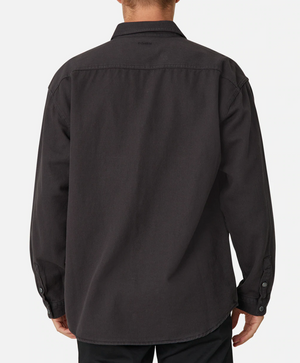 A person wearing the Industrie The Portland Shirt, a stylish, long-sleeved black button-up crafted from a cotton/linen blend, stands facing away from the camera against a plain white background. The shirt features an Industrie logo on the collar, buttoned cuffs, and a slightly curved hem.