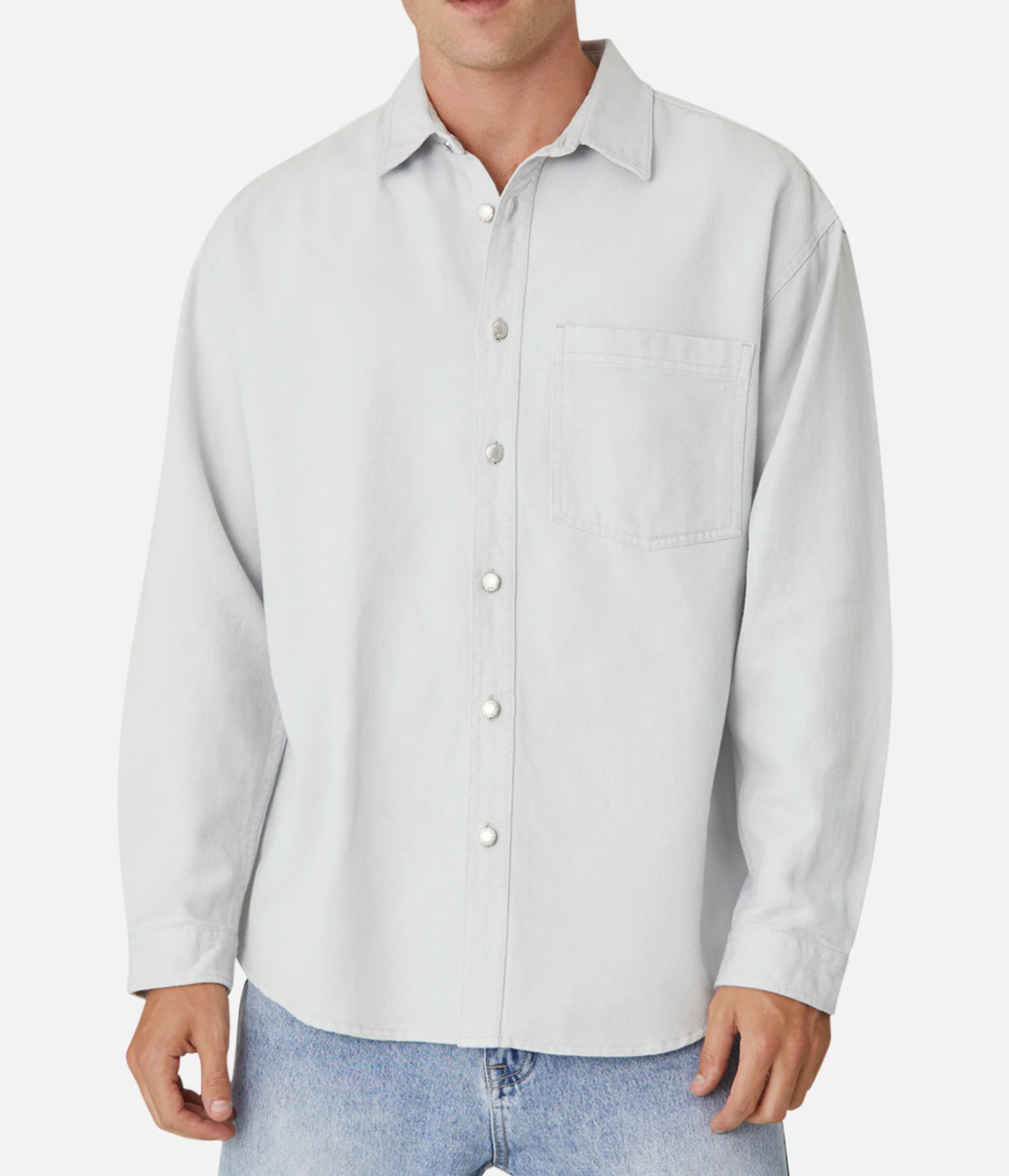 A person is wearing the Industrie The Portland Shirt, a light gray, button-up long-sleeve shirt with a collar and a pocket on the left side of the chest featuring the Industrie logo. This stylish shirt is paired with light blue jeans. The person's head is not visible in the image.