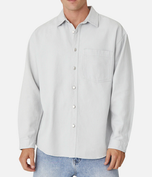 A person is wearing the Industrie The Portland Shirt, a light gray, button-up long-sleeve shirt with a collar and a pocket on the left side of the chest featuring the Industrie logo. This stylish shirt is paired with light blue jeans. The person's head is not visible in the image.