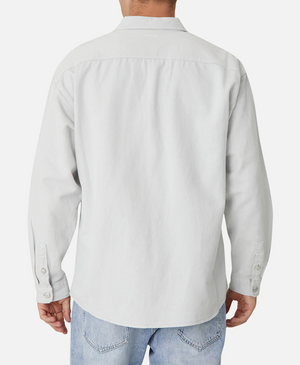 A person is standing with their back facing the camera, wearing a stylish Industrie The Portland Shirt in light gray, made from a Cotton/Linen blend, and light blue jeans. The shirt features a collar and buttons on the cuffs and subtly displays the Industrie logo. The background is white.