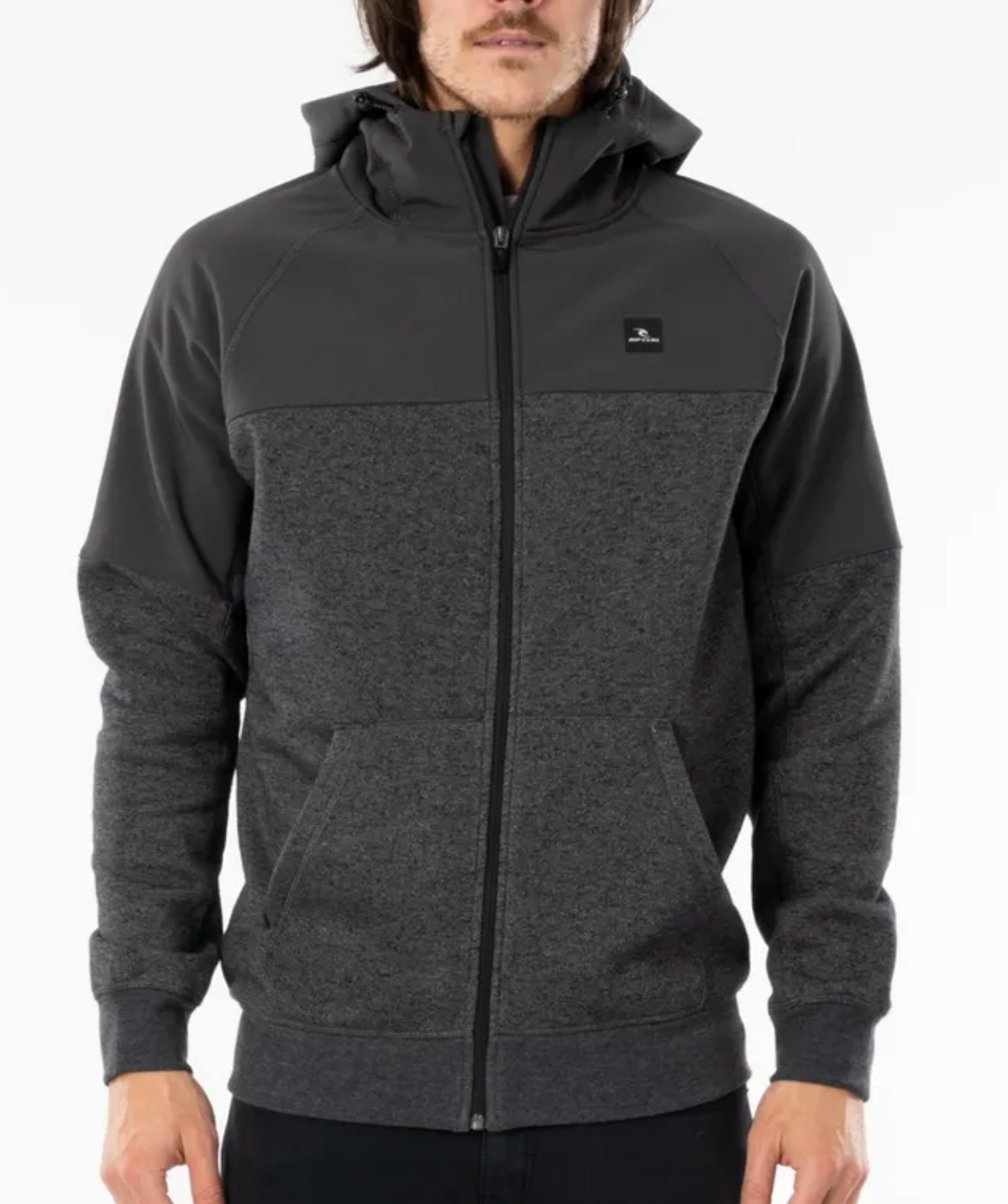 A person with long hair is wearing a Rip Curl Viral Anti Series Zip Thru Hood in dark grey, featuring a lighter grey midsection and kangaroo pockets. The durable water-resistant hoodie has a small black square logo on the left chest. The background is plain white.