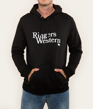 A person is dressed in a Ringers Western Lodge Hoodie, featuring a black color with "Ringers Western" printed in white on the front. This comfy hoodie includes a front pocket where the individual has both their hands tucked inside. Completing their look, they are wearing blue jeans against a plain, light-colored background.
