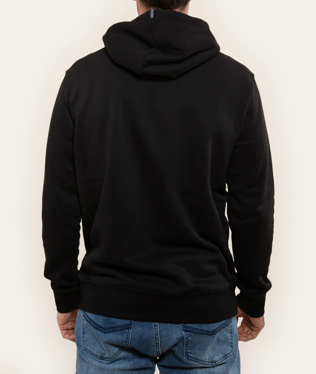 A person in a comfortable, relaxed fit Ringers Western Lodge Hoodie in black and blue jeans is shown from the back. The hoodie hood is down, and the person's hands are relaxed by their sides. The background is a plain light color.