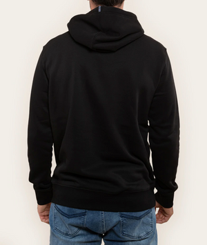 A person in a comfortable, relaxed fit Ringers Western Lodge Hoodie in black and blue jeans is shown from the back. The hoodie hood is down, and the person's hands are relaxed by their sides. The background is a plain light color.