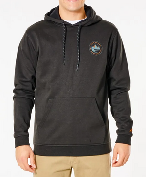 A person wears the black Rip Curl Anti Series Journey Hood, featuring a small circular left chest logo, front pocket, and Durable Water Resistant fabric, paired with beige pants, standing against a plain white background.
