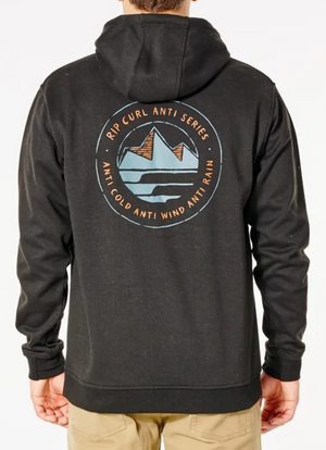 A person wearing the Rip Curl Anti Series Journey Hood, a black jacket with a circular mountain logo on the back. The text reads "Rip Curl Anti Series" and "Anti Cold, Anti Wind, Anti Rain." They stand facing away, hands in pockets.