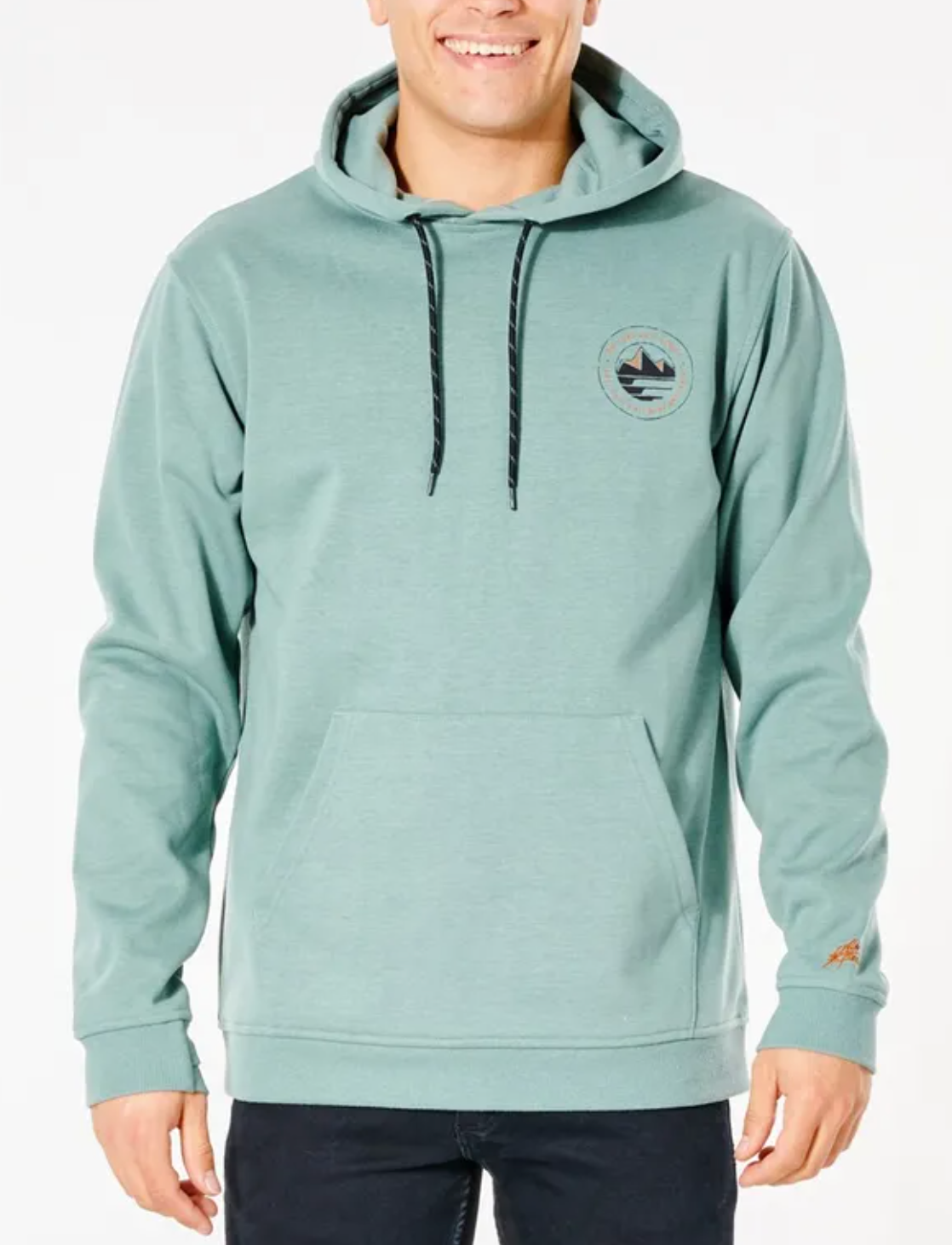 A person smiles while wearing black pants and a light green Rip Curl Anti Series Journey Hood, featuring a mountain and wave logo. The durable water-resistant hoodie has black drawstrings, a kangaroo pocket, and is part of the winter clothing line.