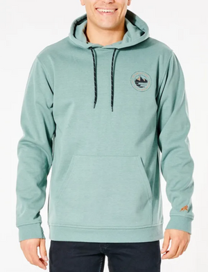 A person smiles while wearing black pants and a light green Rip Curl Anti Series Journey Hood, featuring a mountain and wave logo. The durable water-resistant hoodie has black drawstrings, a kangaroo pocket, and is part of the winter clothing line.