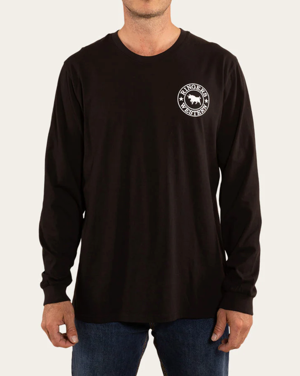 A person wearing the Ringers Western Signature Bull Loose Fit L/S T-Shirt, made of comfortable 100% cotton and featuring a circular "Ringers Western" logo on the left chest, pairs it with blue jeans against a plain, light-colored background.