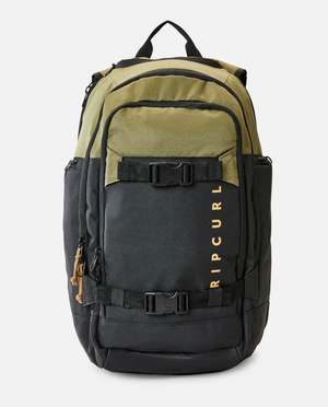 The Rip Curl Posse 33L Overland Backpack is a durable, multicolored bag featuring olive green and black panels made from recycled polyester. It boasts multiple compartments, a handy internal laptop section, black adjustable straps, and a prominent orange "Rip Curl" logo on the front. The top handle is black, along with the visible zippers and buckles.