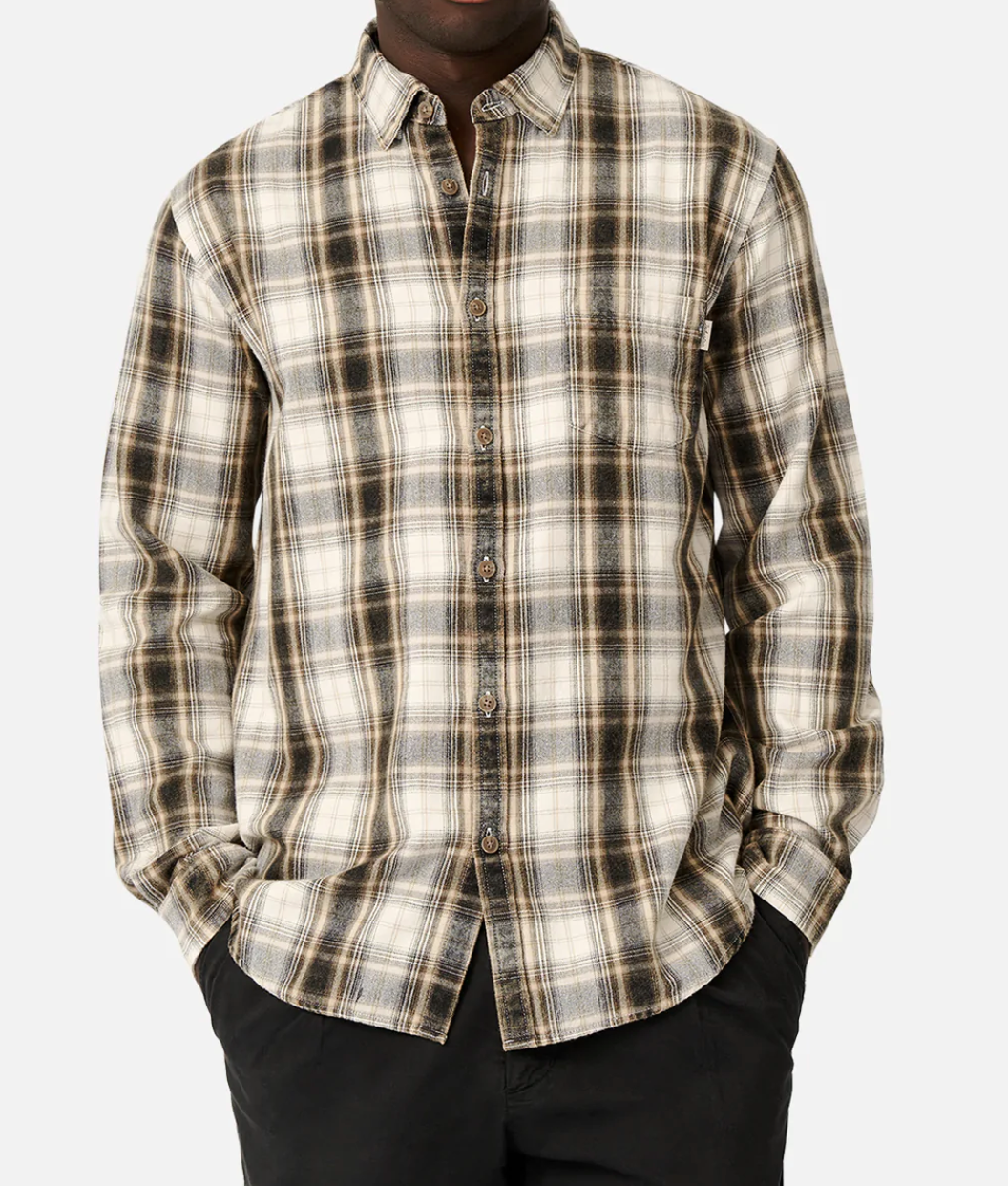 A person wearing the comfortable Industrie The Cedar Oaks Shirt, featuring a beige, black, and white plaid pattern made of 100% cotton, stands against a plain white background with their hands in the pockets of their black pants. The casual button-up shirt includes a chest pocket and is worn slightly open at the top.