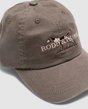 The Rodd & Gunn Double Barrel Cap in brown showcases an embroidered hunting dog logo and "RODD & GUNN" text on the front. Made from durable cotton twill, it features a curved brim and prominent stitching for a stylish yet sturdy design.