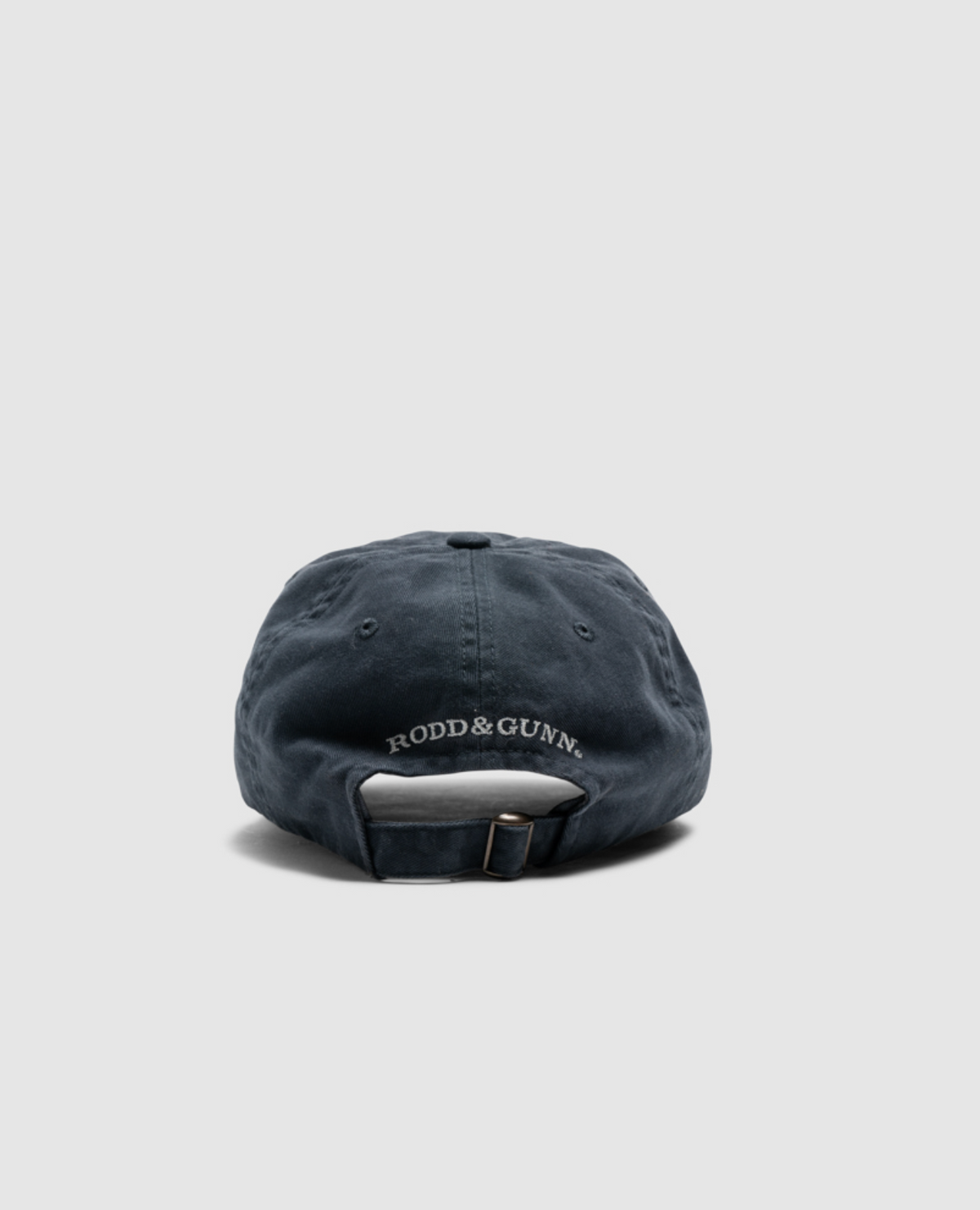 Back view of the Rodd & Gunn Double Barrel Cap in dark blue heavy-duty cotton twill, featuring "RODD & GUNN" embroidered in white. The cap has an adjustable strap with a metal buckle on a light gray background.