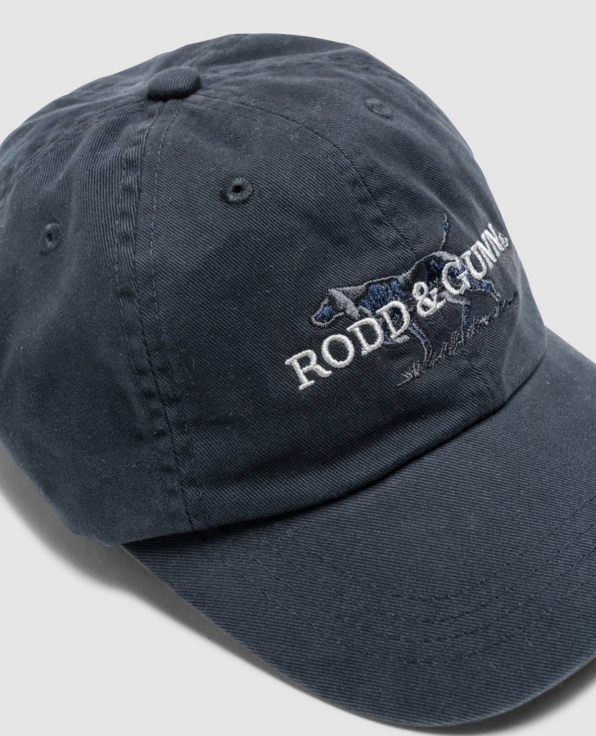 Introducing the Rodd & Gunn Double Barrel Cap in dark blue, made from durable cotton twill. This stylish accessory showcases embroidered "RODD & GUNN" text and a dog logo on the front. Featuring a curved brim and visible stitching, it's ideal for those who appreciate style and longevity.