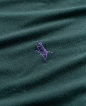 The Rodd & Gunn The Gunn T-Shirt in dark green, made from premium Australian Cotton, showcases a purple embroidered logo of a walking dog or horse. Its comfortable sports fit merges casual style with understated elegance.