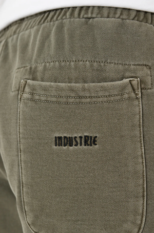 A close-up of the olive green Industrie The Del Sur Track Short reveals a pocket with "INDUSTRIE" embroidered above it in black thread. Its elastic waistband hints at an oversized fit, ideal for a relaxed track short style.