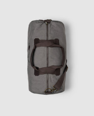 The Rodd & Gunn Double Barrel Duffle Bag in gray cotton canvas has dark brown straps, a zippered closure, and is shown on a plain white background. It features a detachable shoulder strap connected with sturdy metal rings.