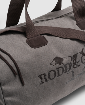Close-up of the Rodd & Gunn Double Barrel Duffle Bag in gray cotton canvas with brown handles and a partial dog logo, featuring stylish functionality and durability for any adventure.