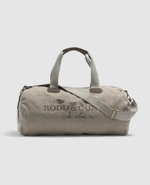 The beige Rodd & Gunn Double Barrel Duffle Bag features a dark logo, dual handles, and a detachable shoulder strap. It includes metal zippers and buckles, stands upright against a light gray background, and is ideal for travel.