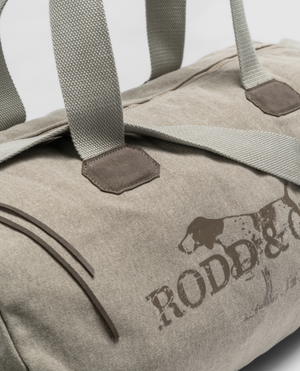 The Rodd & Gunn Double Barrel Duffle Bag is made of durable cotton canvas with gray straps and a dog illustration beside "RODD & GUNN." It sits angled on a white background, blending elegance with practicality in its beige design.