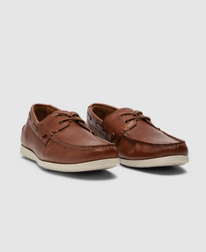 The Rodd & Gunn Gordons Bay Boat Shoe, crafted from brown leather, features intricate stitching, laces, and off-white rubber outsoles. These casual boat shoes are displayed on a light gray background, angled slightly outward.