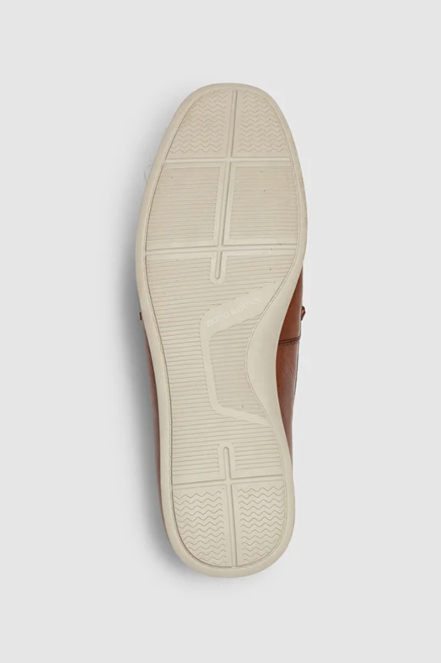 The Rodd & Gunn Gordons Bay Boat Shoe showcases a white textured rubber outsole with a central groove and diagonal tread patterns, complemented by a brown leather upper visible on the sides.