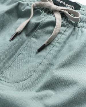 The Rodd & Gunn Resort Short in light teal features an elastic waist, pockets, and visible stitching. Made from a cotton-elastane blend, it includes gray drawstrings with metallic tips. The brand name is partially visible at the top.