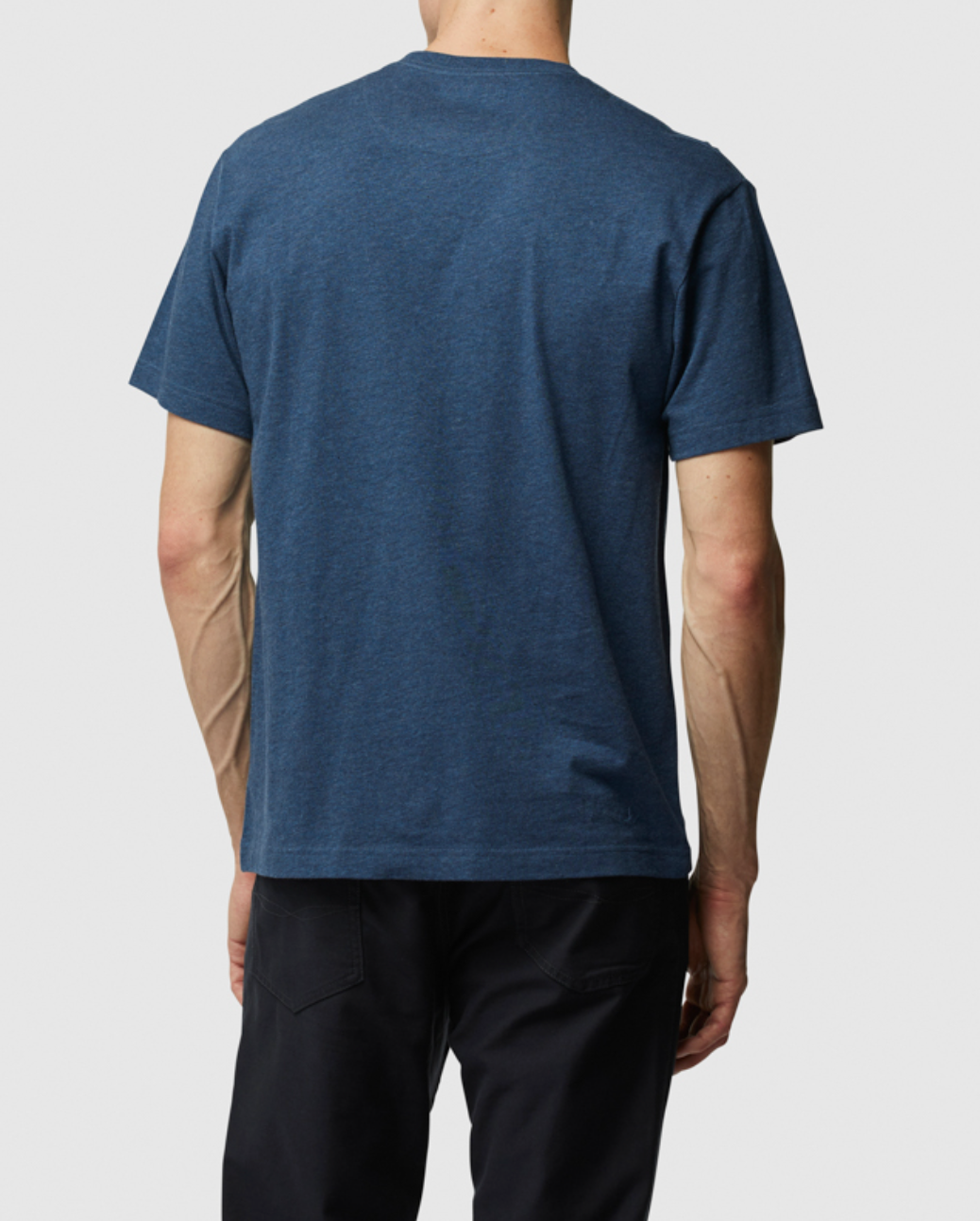 Wearing a blue Rodd & Gunn The Gunn T-Shirt made of soft Australian Cotton and black pants, someone is seen from the back against a white background. The tee boasts a sports fit, combining clean design with comfort and style.