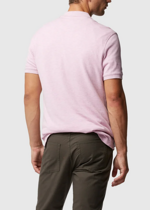 A person faces away, highlighting the modern fit of the Rodd & Gunn The Gunn Polo made from Australian cotton in light pink, paired with dark olive green pants. A plain light gray background offers a minimalist setting for this fashionable look.