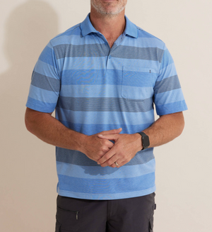 A person dressed in the Breakaway Retba Kinnersly Polo—a blue and gray striped shirt with a ribbed collar—stands against a plain background. Their arms are loosely crossed, paired with dark pants and a wristwatch, while the polo's short sleeves are neatly styled; their head isn't visible.
