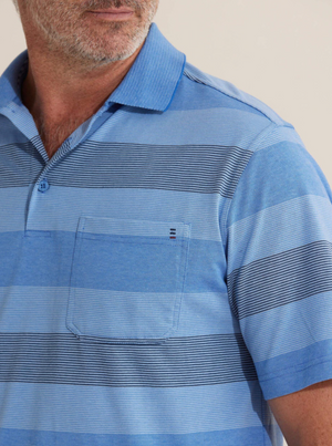 A man stands against a plain background wearing the Breakaway Retba Kinnersly Polo, featuring blue horizontal stripes, short sleeves, a rib knit collar, and a chest pocket. His face is partially visible in the scene.