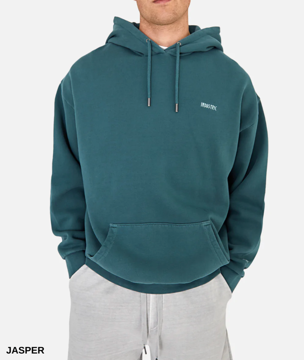 A person in an oversized teal Industrie The Del Sur Hoodie with "INDUSTRIE" on the chest, front pocket, and drawstrings, paired with light gray sweatpants against a plain white background.