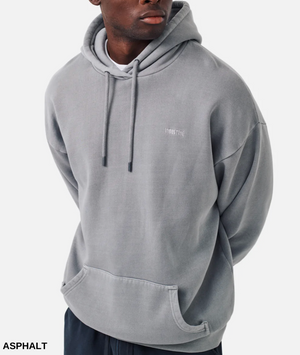 A person in a cozy, oversized acid-washed gray hoodie with a small chest logo, drawstrings, and a front pocket from Industrie The Del Sur Hoodie collection paired with black pants stands against a plain white background.