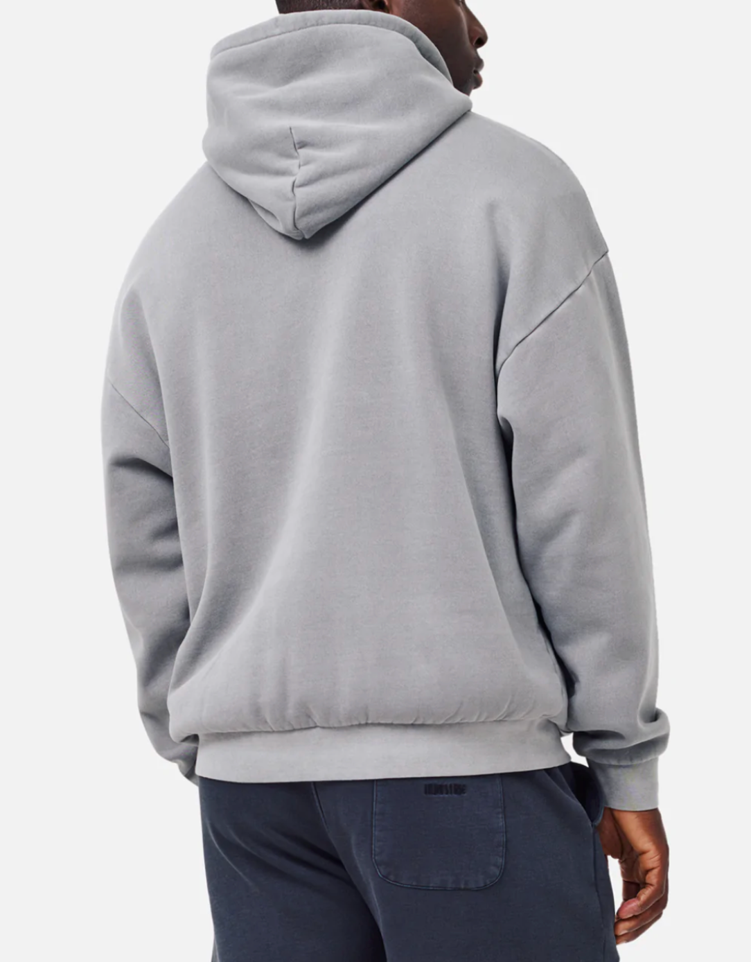 A person wears the Industrie The Del Sur Hoodie in acid wash light gray with dark gray pants. Their right hand is partially visible, and the hood is up, covering their head. The oversized comfy fit gives a relaxed vibe against the plain white background.