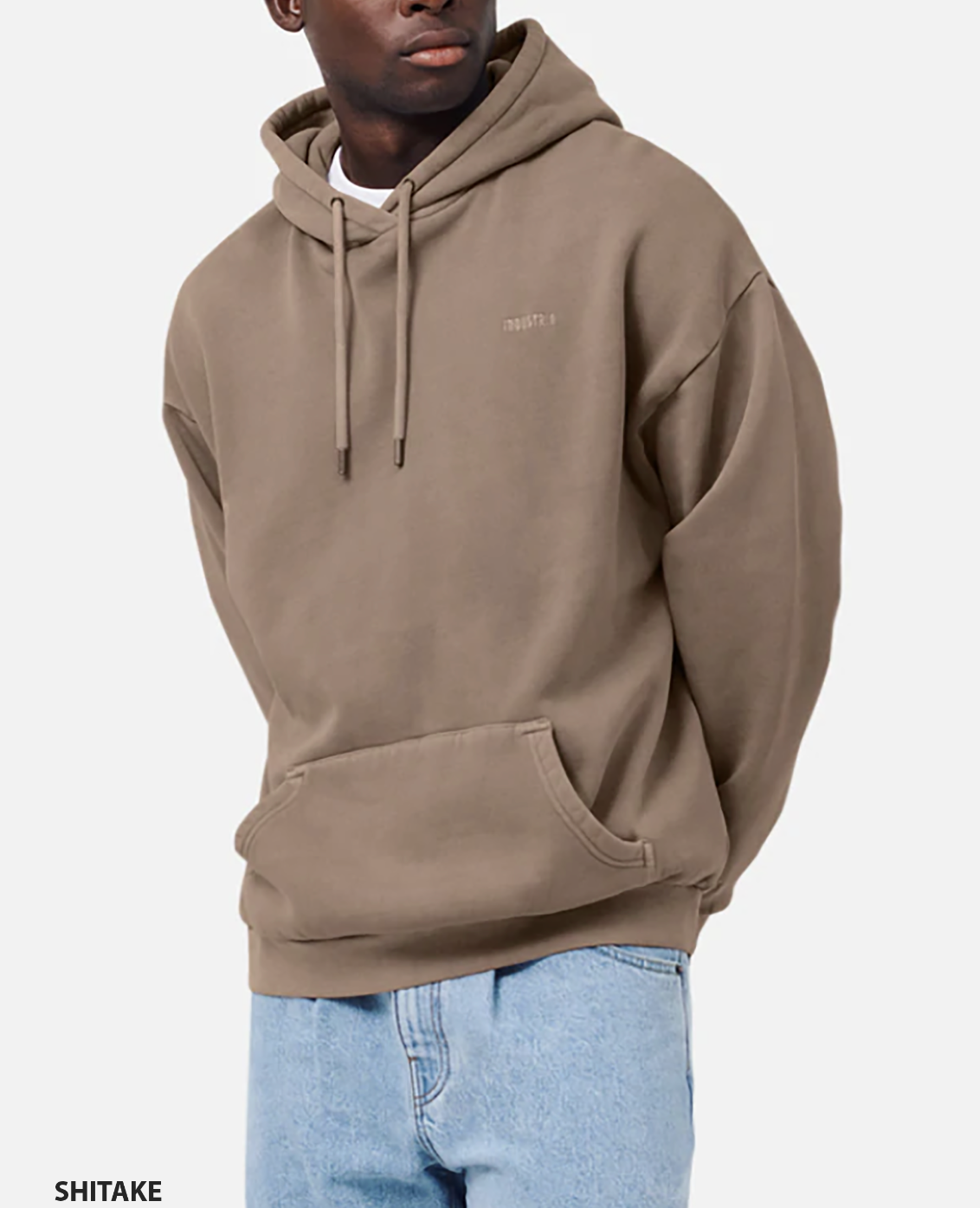 A person models the Industrie The Del Sur Hoodie, an oversized brown sweatshirt with drawstrings and a front pocket. "SHITAKE" is seen in the bottom left corner. They pair it with light blue jeans for a laid-back style against a plain white backdrop.