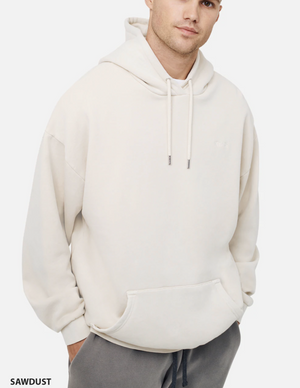 A person wears the Industrie The Del Sur Hoodie, an oversized light beige hoodie with a front pocket and drawstrings, paired with dark pants. The background is plain white, featuring "SAWDUST" text in the bottom left corner.