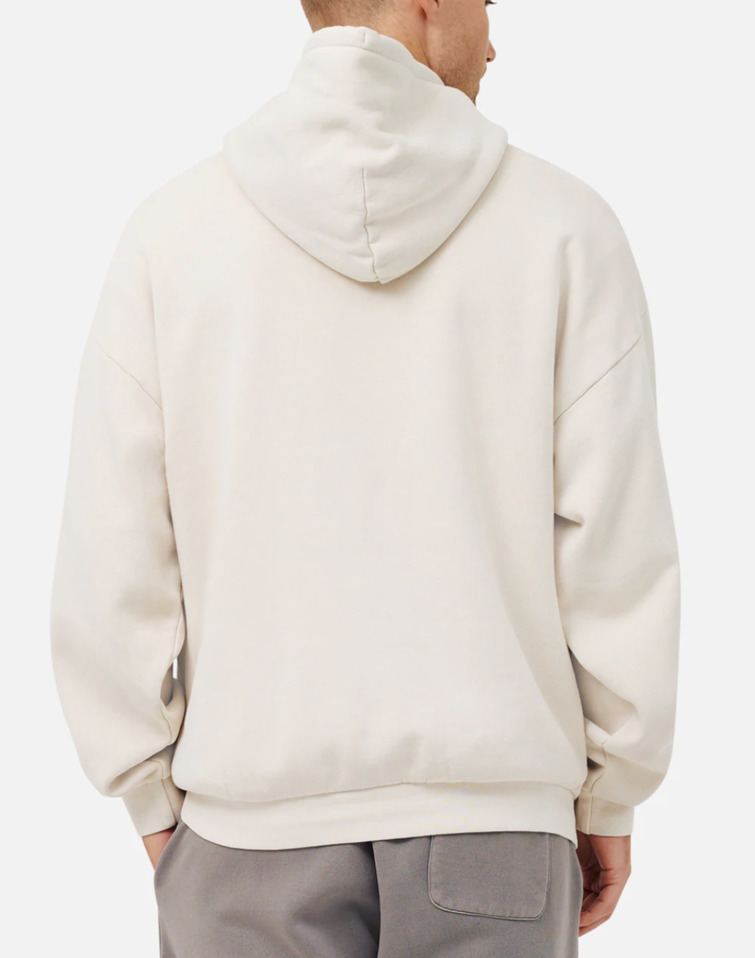 Facing away from the camera, a person dons the Industrie The Del Sur Hoodie in an oversized cream fit with a raised hood and slightly long sleeves. Gray pants complement the look against a plain white backdrop, highlighting its relaxed style.
