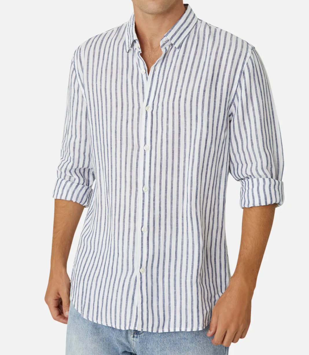 A person is wearing the Industrie The Feliz Shirt, a classic fit, 100% linen shirt in white with vertical blue stripes, rolled-up sleeves, a collar, and buttons down the front. They pair it with light blue jeans against a plain white background.