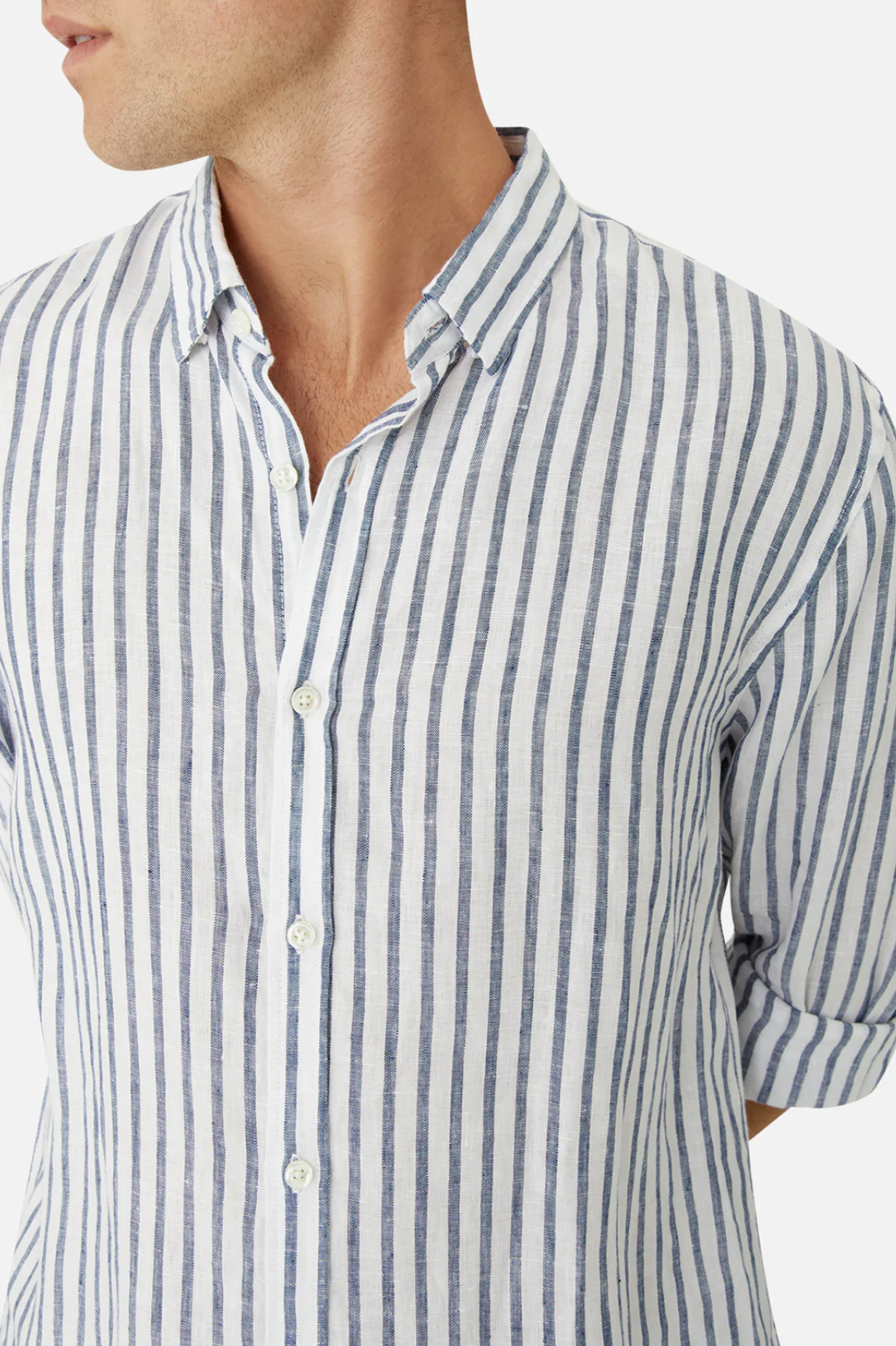 A person wears the Industrie The Feliz Shirt, a classic fit button-up with blue and white vertical stripes, made from 100% linen. The rolled-up sleeves enhance its comfort appeal, shown against a plain white background focusing from shoulders to waist.