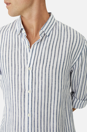 A person wears the Industrie The Feliz Shirt, a classic fit button-up with blue and white vertical stripes, made from 100% linen. The rolled-up sleeves enhance its comfort appeal, shown against a plain white background focusing from shoulders to waist.