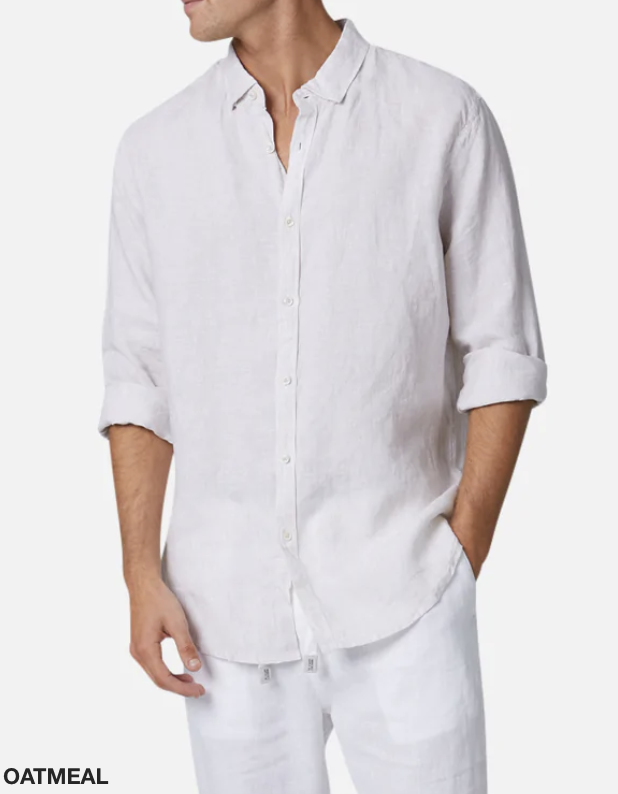 A man wearing the Industrie The Rochecroft Shirt in a light oatmeal color, with the long sleeves rolled up. The relaxed fit and 100% linen material exude comfort. Paired with light-colored pants, his left hand rests in his pocket against a plain white background. The word "OATMEAL" is written in the bottom left corner.