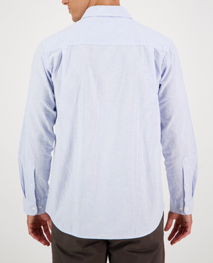 Seen from the back, a person wears a Swanndri Carillo Beach L/S Shirt in light blue with subtle stripes. The comfortable, casual-fit shirt has long sleeves and is tucked into dark pants.