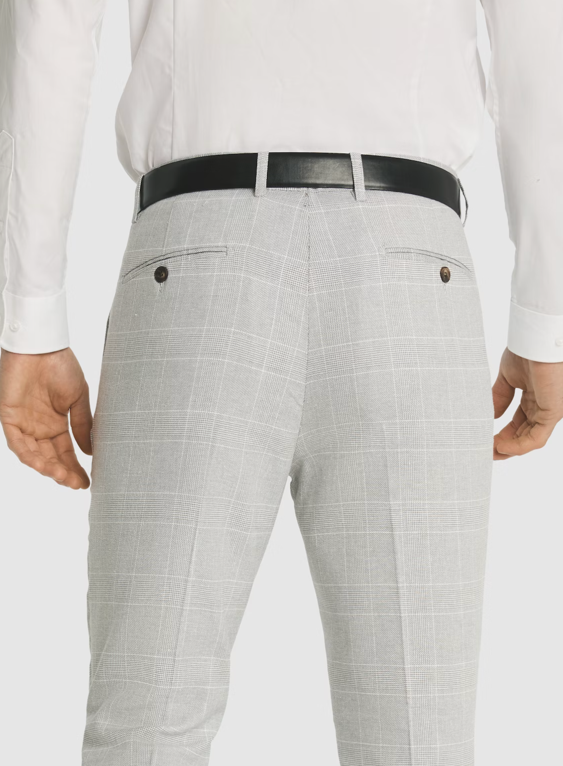 A man is shown from the back wearing a white shirt, black belt, and light gray plaid Connor Sorrento Slim Dress Pant, highlighting its tailored fit and buttoned back pockets.
