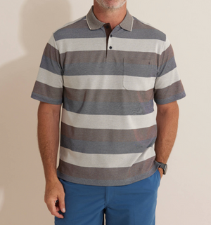 A man wearing the Breakaway Machu Micro Prima Polo with gray and brown horizontal stripes, a rib knit collar, chest pocket, and blue pants stands against a light background.