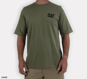 A person in a green CAT Trademark Tee, featuring a black "CAT" logo on the left chest and made from 100% cotton, stands with arms relaxed. The T-shirt pairs seamlessly with light brown shorts against a plain white background.
